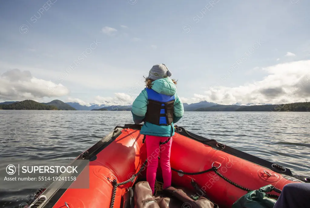 A young girl stands at bow of rubber boat in big bay