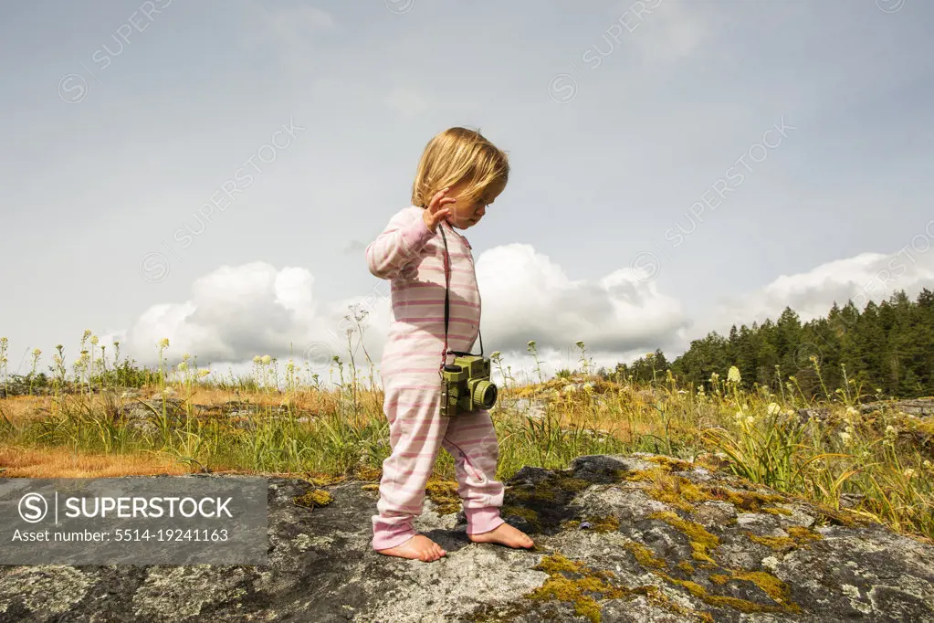 A young child in pajamas with a camera walks on a mossy rock
