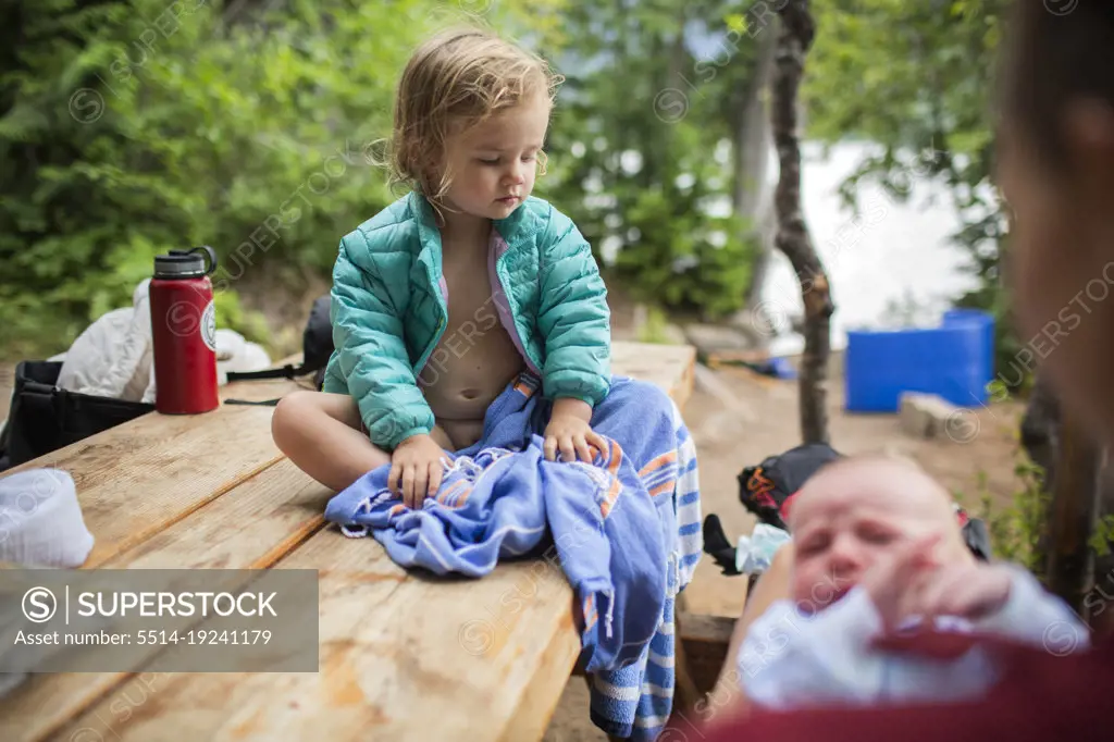 A young child sits on picnic table ta campsite with baby