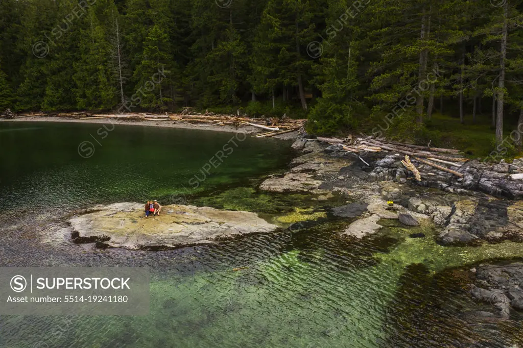 A family sits on rock surrounded by clear green water and forests