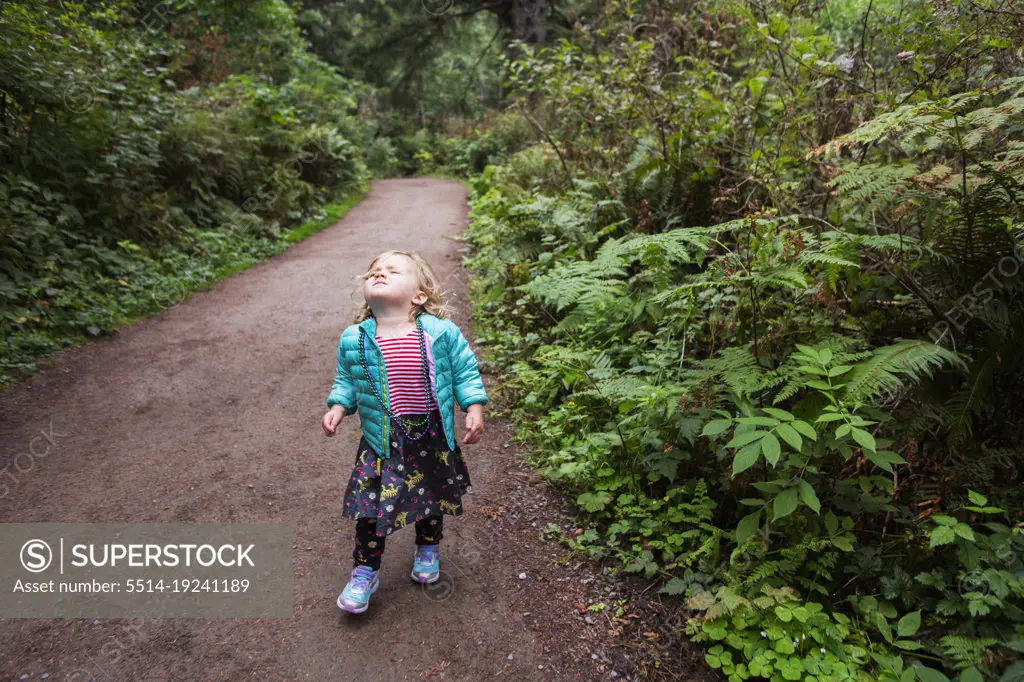 A young girl looks up, eyes closed on forested trail
