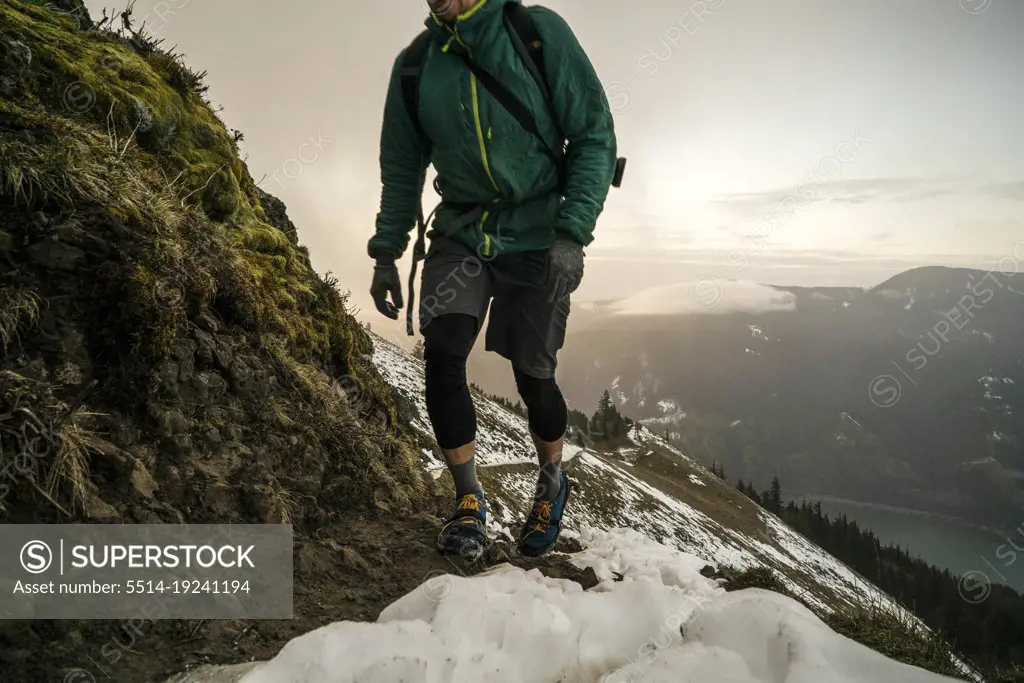 A man hikes up a mountain trail with snow and steep slope in distance