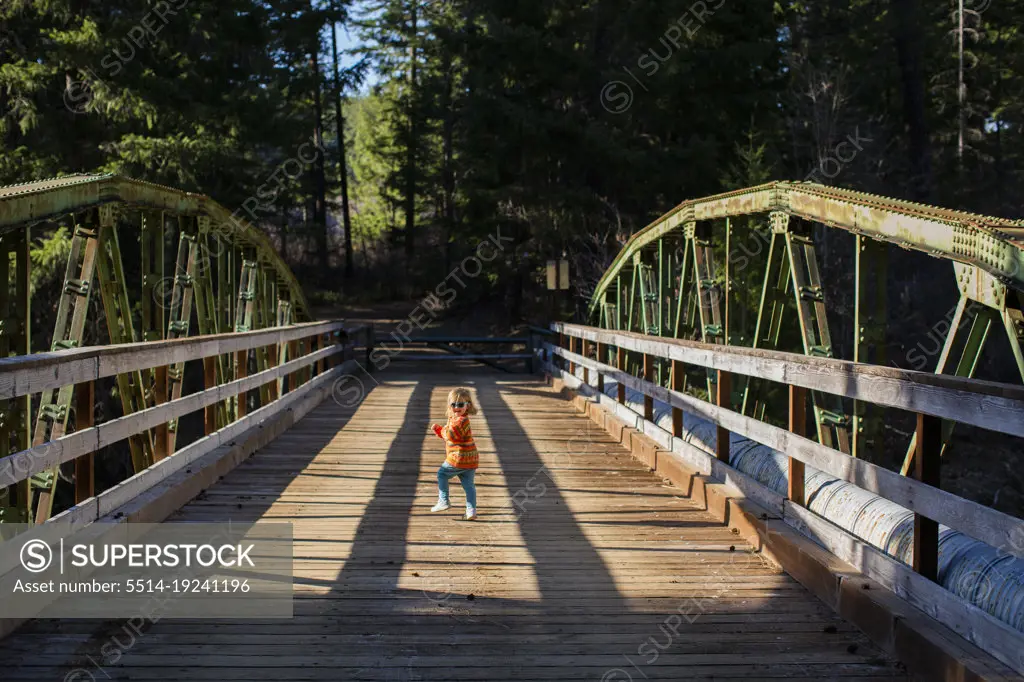 A young girl runs across old wooden bridge in sunshine