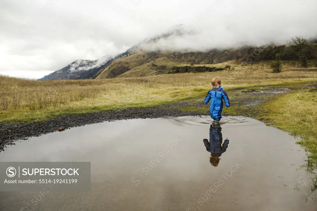 A young child walks through a shallow puddle in a wide landscape