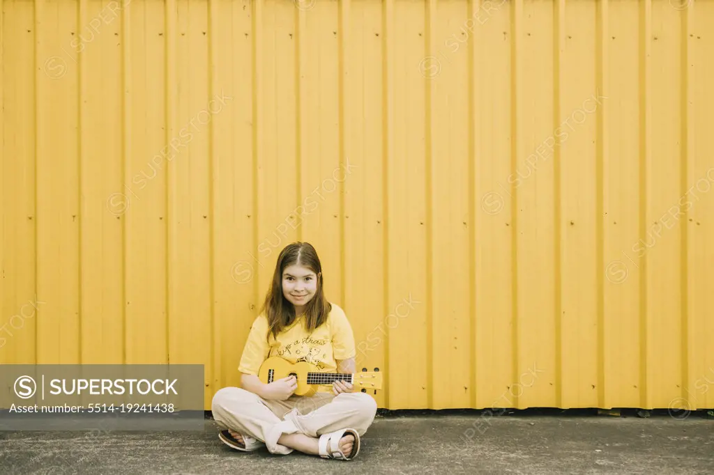 Young girl sitting outside playing a ukulele