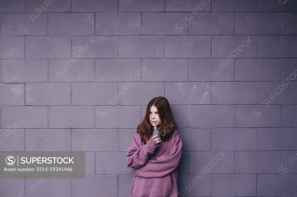 Girl standing against a purple wall drinking a smoothie