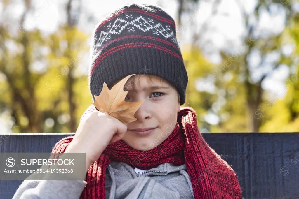 Kid with a leave in his hand, wearing a woolen Hat and scarf. Fall