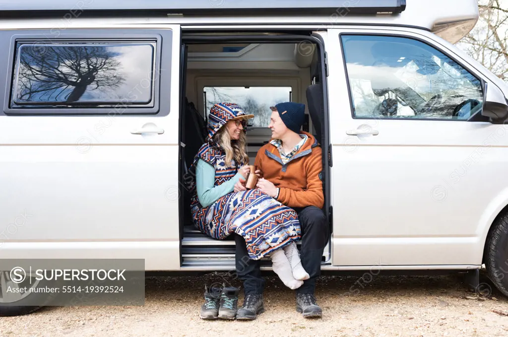 man and woman sat in a campervan enjoying coffee chatting and laughing