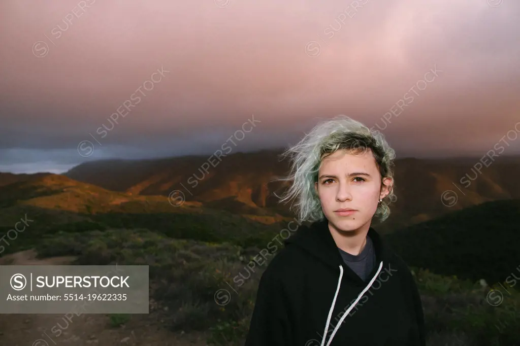 Teen Girl With Blue Hair Under Pink Clouds On Top Of a Mountain