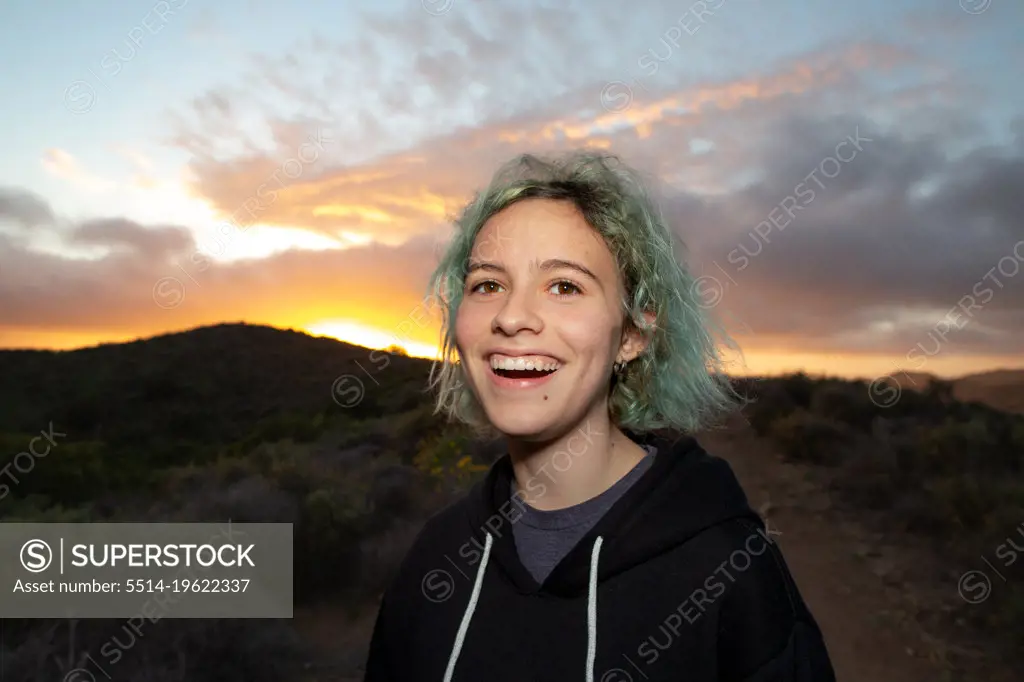 Teen Girl Laughing While On A Hiking Trail With A Sunset Behind Her