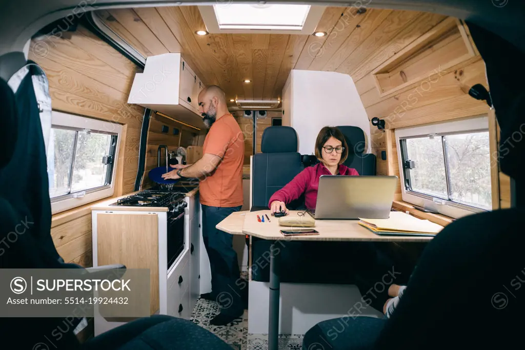 Couple living in a camper van. Woman teleworking. Man washing dishes.