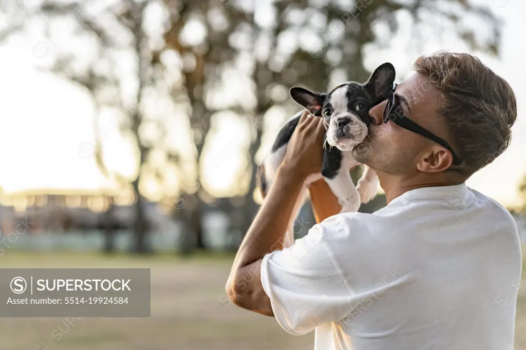 Happy man holding up and kissing a french bulldog.
