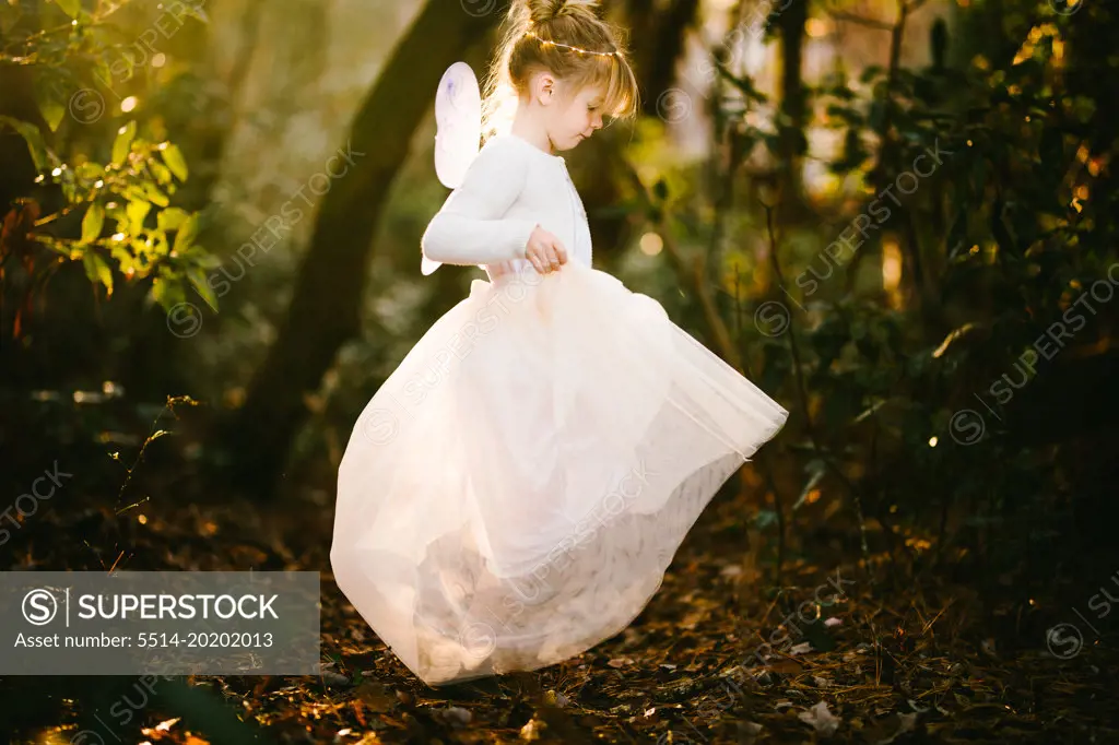 Girl child twirls in golden light in forest in angel costume