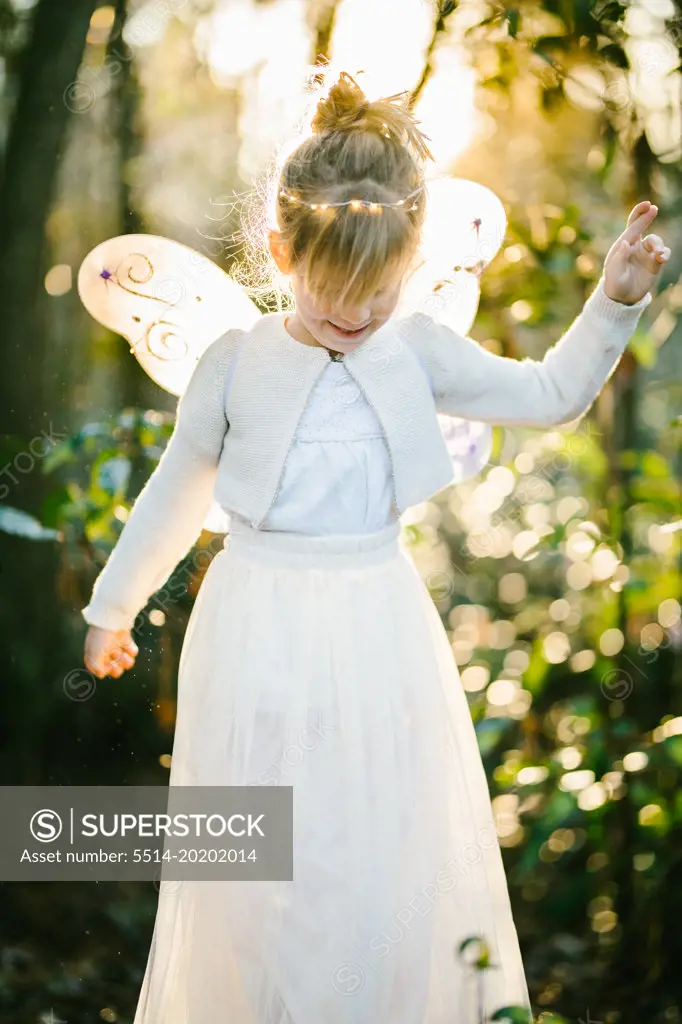 Girl in angel wings with light shining through forest with bokeh