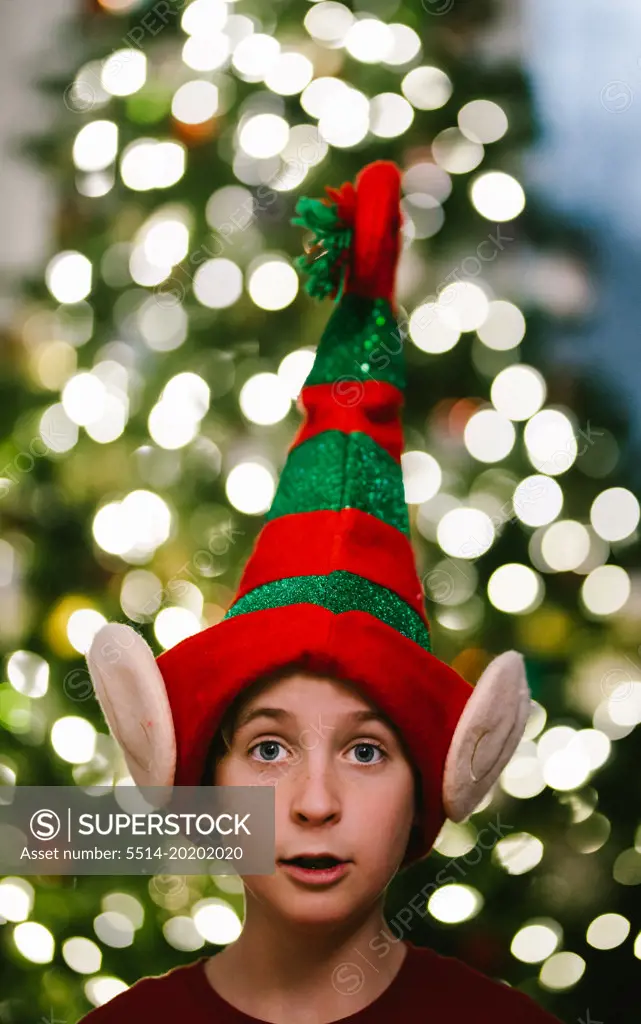 Preteen boy in Christmas elf hat with Christmas tree light bokeh
