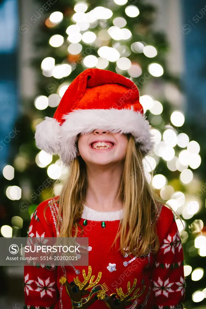 Blond child smiles big in santa hat in front of Christmas tree