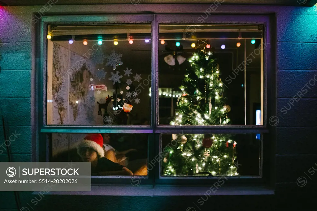 Boy looks out window of home with Christmas tree and Santa hat