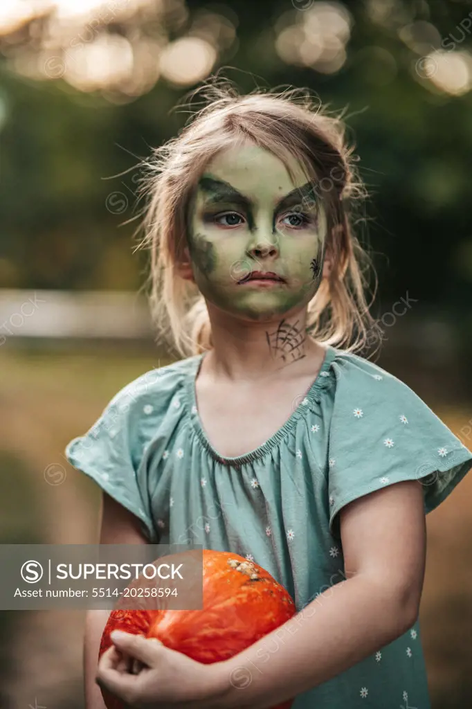 Little girl with witch makeup Halloween party with a pumpkin