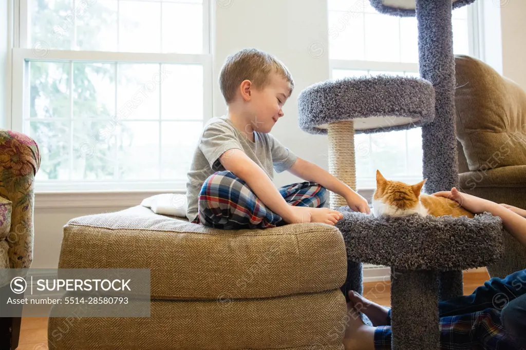 Happy Young Boy Sits Smiling and Playing with Resting Pet Cat
