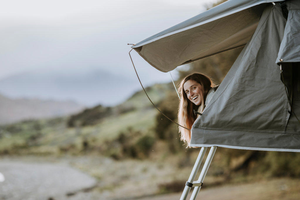 A young smiling woman sticks her head out of a tent in New Zealand.