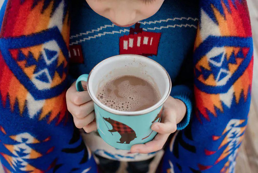 sky view of a boy wrapped in a blanket holding a hot chocolate outside