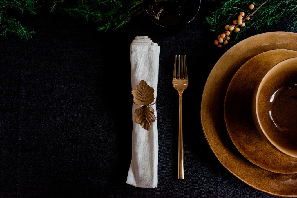 gold napkin holder, plates and fork on a decorated table setting
