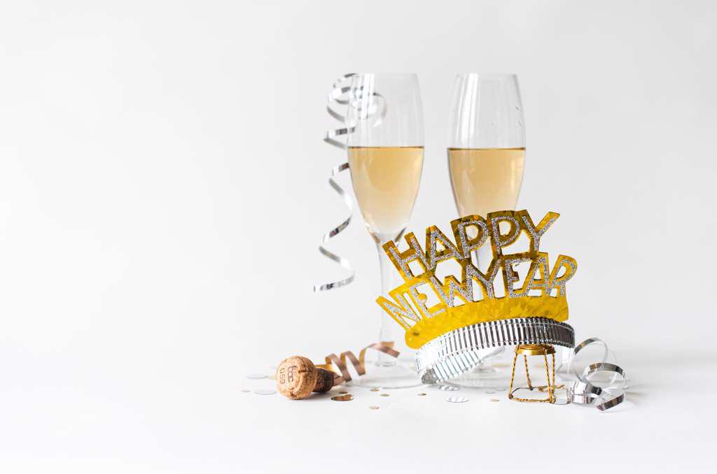Glasses of champagne and Happy New Year hat on white background.