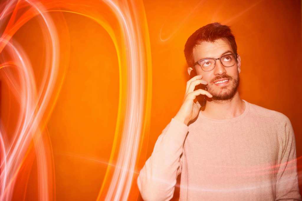 Young man calling with the smartphone on a orange colored background