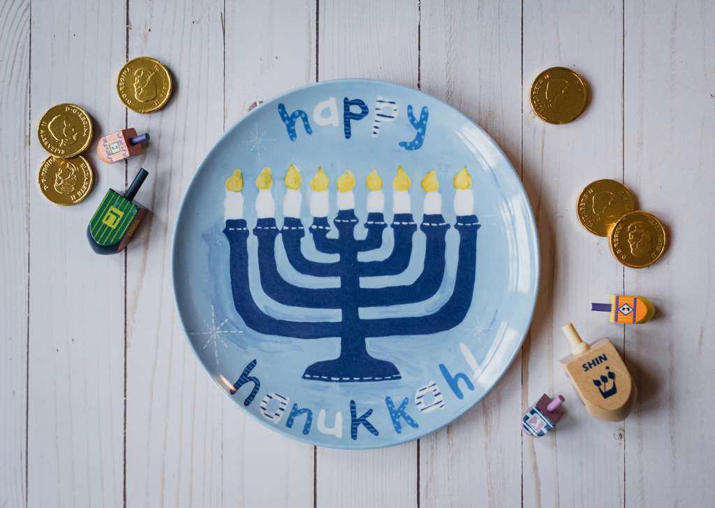 Happy Hanukkah plate, dreidels and chocolate coins on white wood.