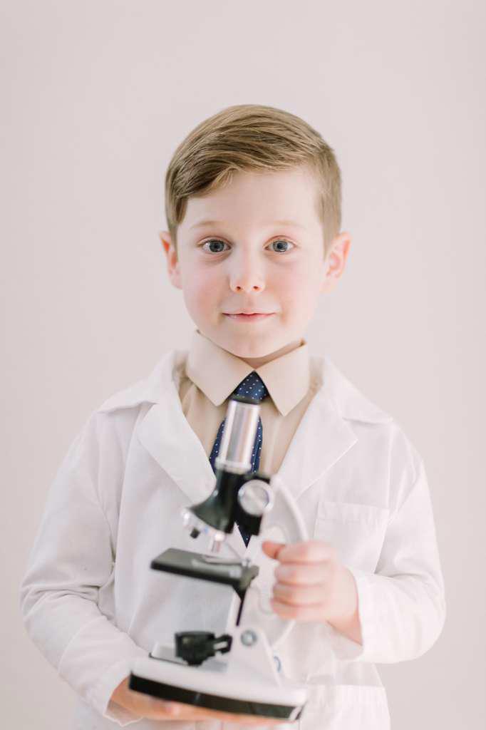 Young child holding a microscope smiling at camera