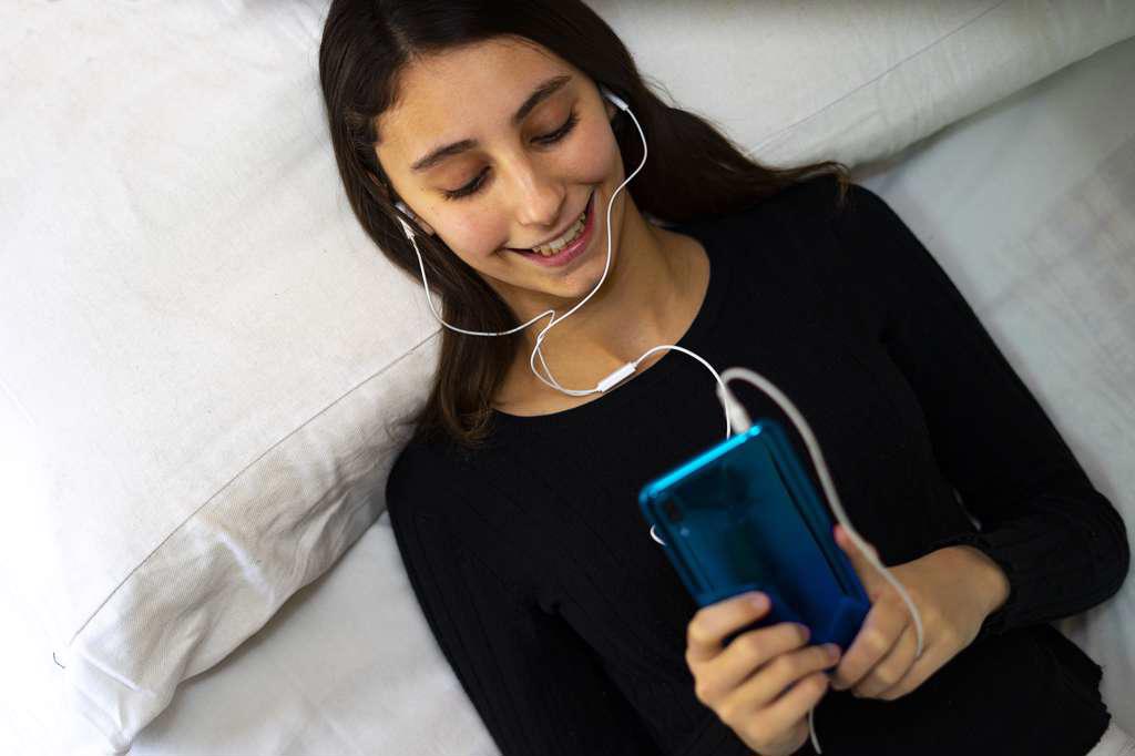 Woman listening to music on a white bed.