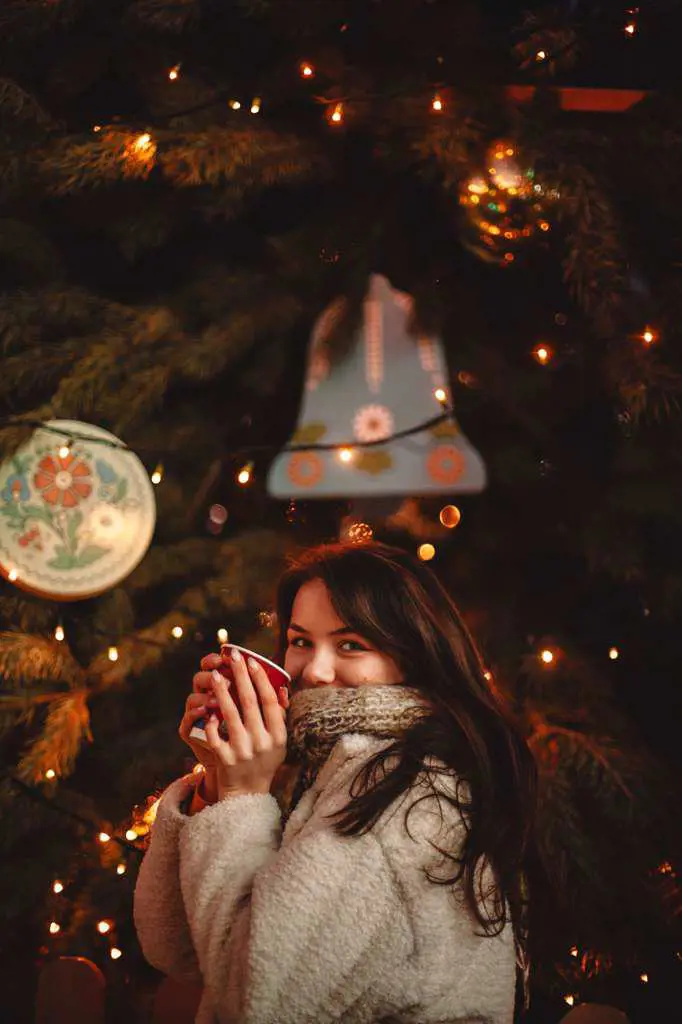 Happy teenage girl holding mulled wine standing by Christmas tree
