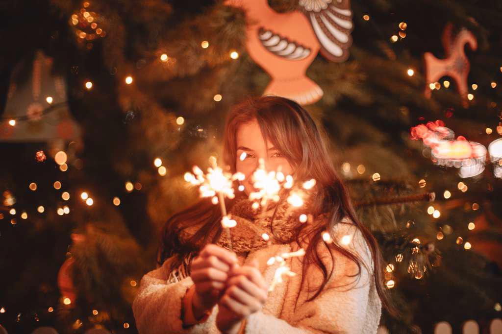 Happy teenage girl holding sparklers standing by Christmas tree
