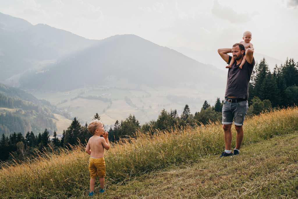 Dad with baby on shoulders looking at young male toddler in mountains