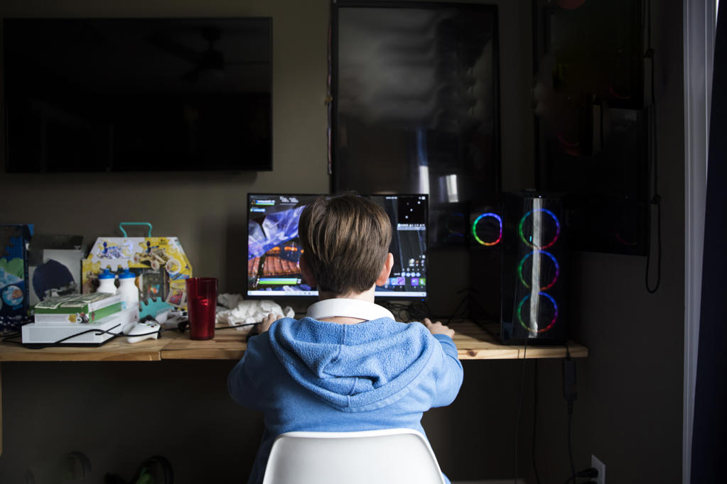 Rear View of Teen Boy Playing On Gaming Computer At Messy Desk