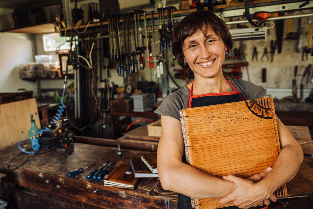 Female artist holding her wooden art work and smiling in a workshop