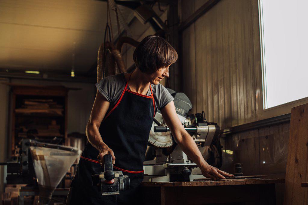 Middle aged woman with power planer in a wood shop