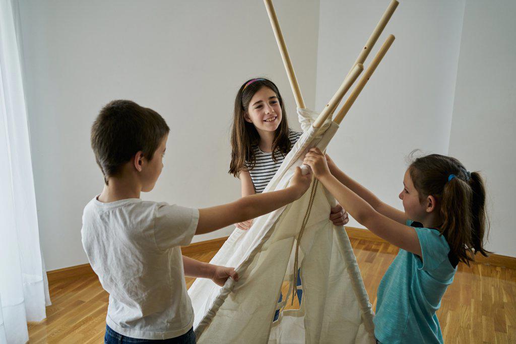 Children putting the sticks to build a teepee tent inside their house. Creativity concept