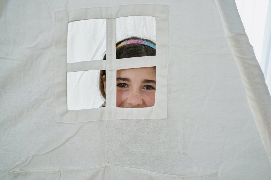 Young girl looking through a window at a white teepee tent. Creative concept