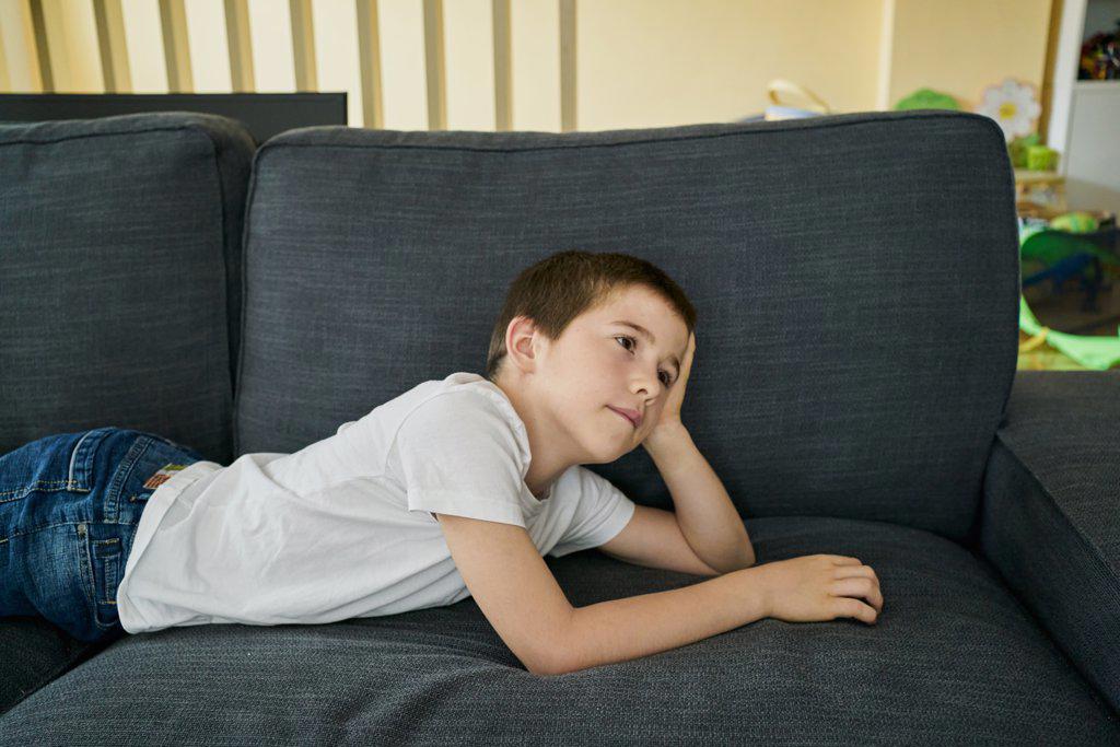 boy with a thoughtful attitude lying on a sofa