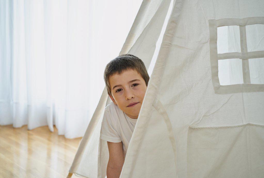 Young boy looking through a window at a white teepee tent. Creative concept