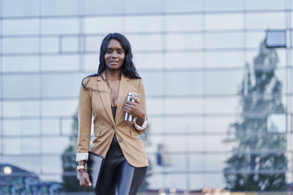 front view portrait of black woman wearing a brown suit talking on the phone and holding a container with coffee in the street