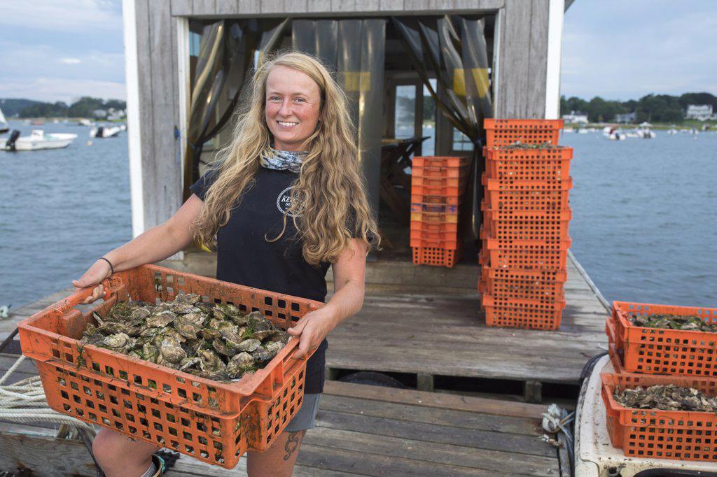 Female shellfish farmer carrying crate of oysters