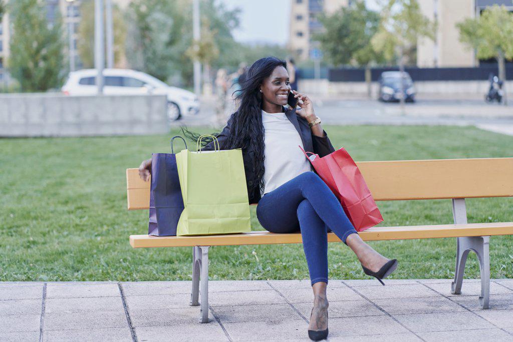 Young black woman talking on smartphone sitting in a park with r
