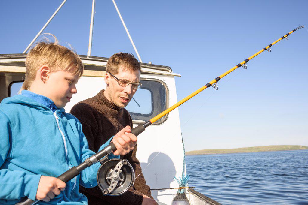 Male fisher teaching boy fishing on boat