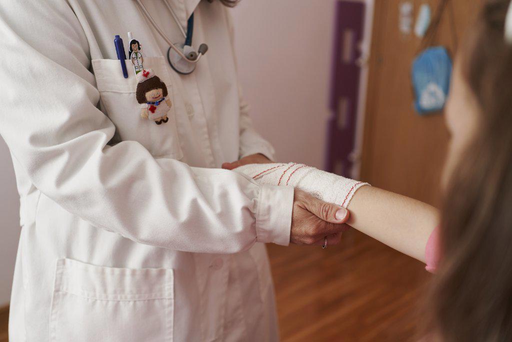 side view of a female doctor bandaging the arm of a little girl in her room. Home doctor concept