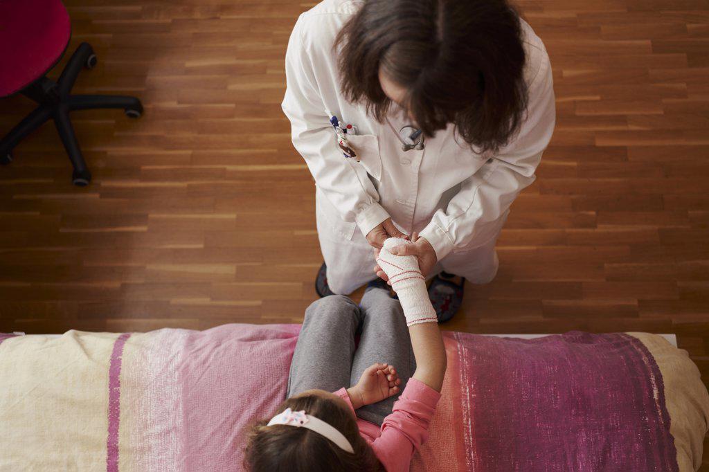 Top view of female doctor bandaging the arm of a little girl in her room. Home doctor concept