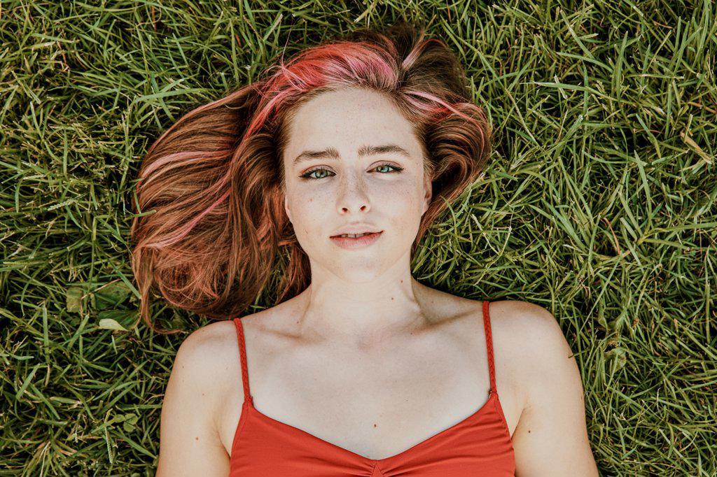 Portrait of young woman lying outdoors on grass.