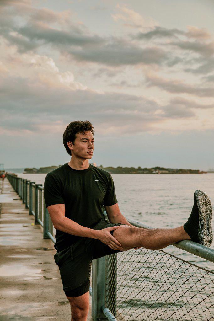 Male athlete stretching on waterfront during sunset.