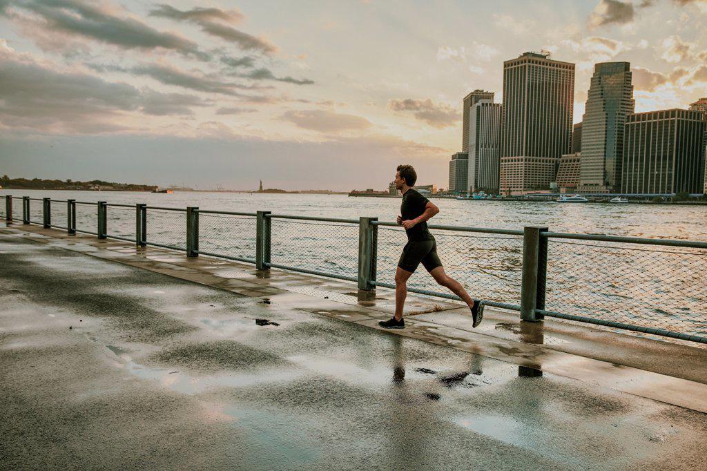 Male athlete running on waterfront during sunset.